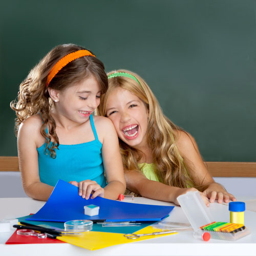 Two girls smiling and having fun as they participate in group French activities in a classroom.