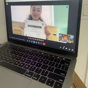 Picture of a laptop with a girl showing a certificate on a zoom call.