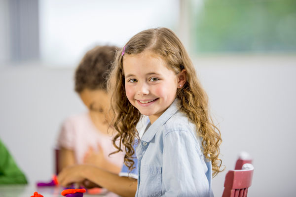 A young girl in a blue shirt smiling as she partakes in French Classes in San Diego.