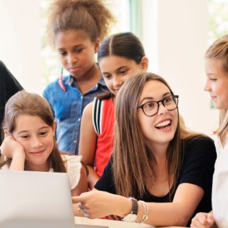 French teacher in a classroom surrounded by several kids participating in French activities.